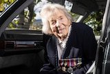 An elderly woman sitting in a car wearing several war medals.