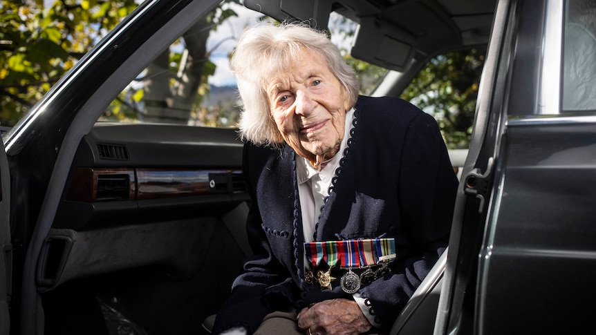 An elderly woman sitting in a car wearing several war medals.