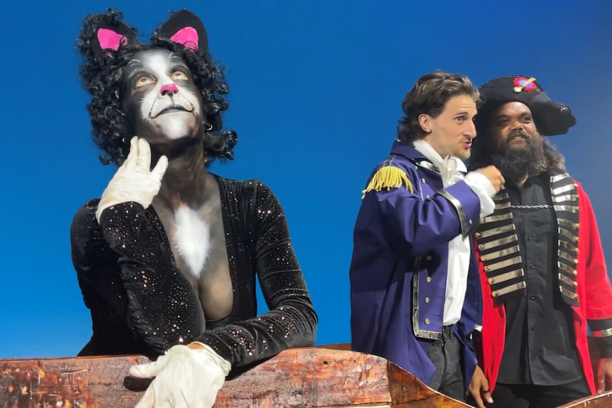 Woman dressed as cat with makeup in foreground and two men talking in background