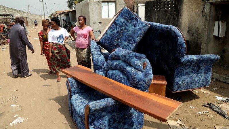 women stand next to coaches that are moved out of a house in Ivory coast.