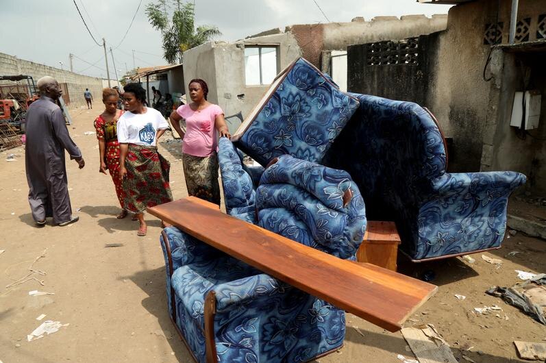 women stand next to coaches that are moved out of a house in Ivory coast.