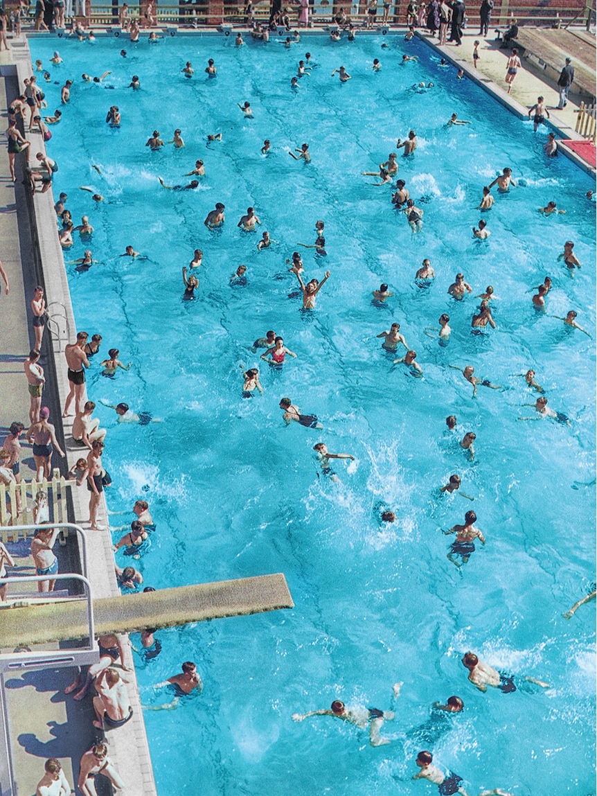 Dozens of people are seen swimming and splashing in a colourised historical photograph of the Adelaide City Baths in 1940.