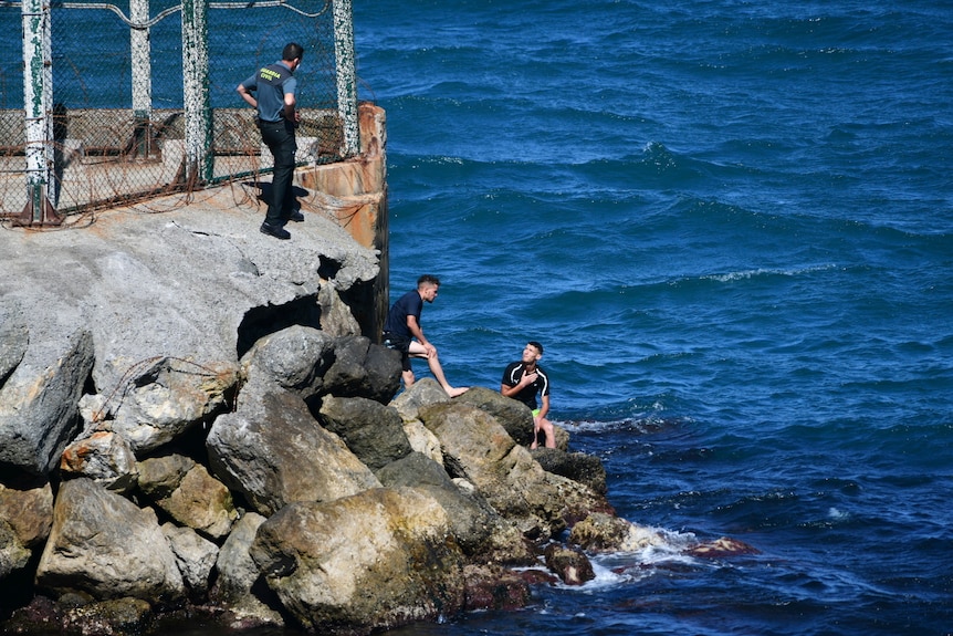 A Spanish Guardia Civil officer stands next to a group of men from Morocco who are trying to cross into the Spanish territory.