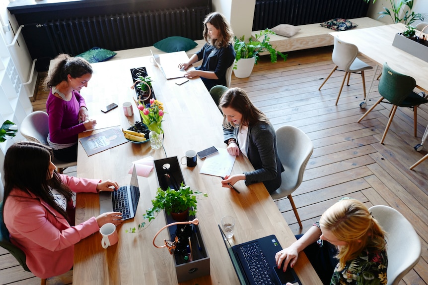 Women working on laptops or documents at a shared table in an office