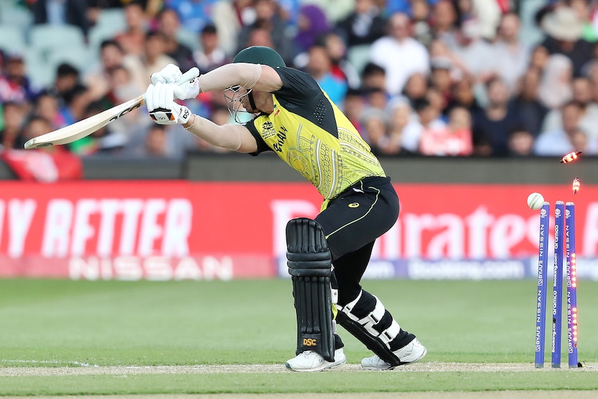 David Warner plays a drive as the ball hits the stumps behind him