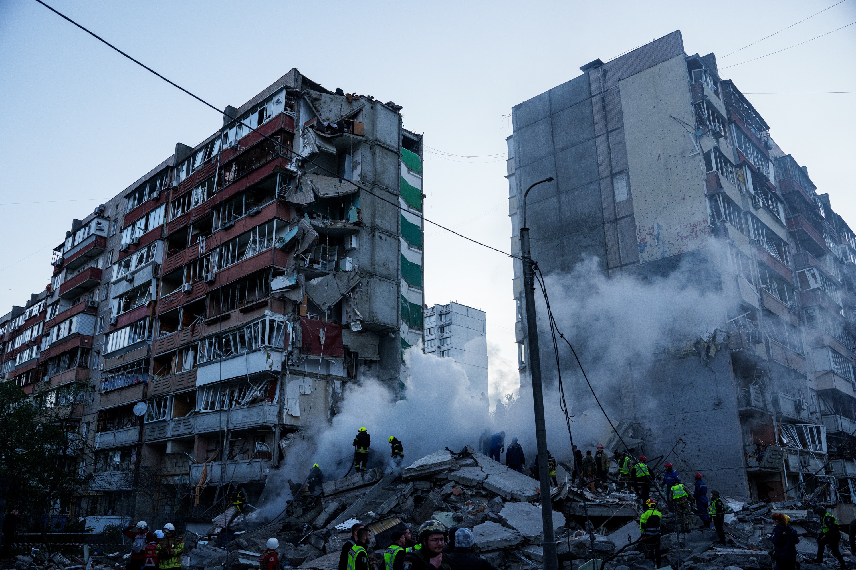 A partially collapsed large Soviet-era apartment building with debris and smouldering rubble.