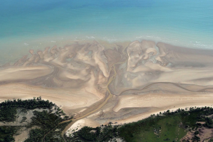 an aerial shot of a creek flowing into a blue sea.