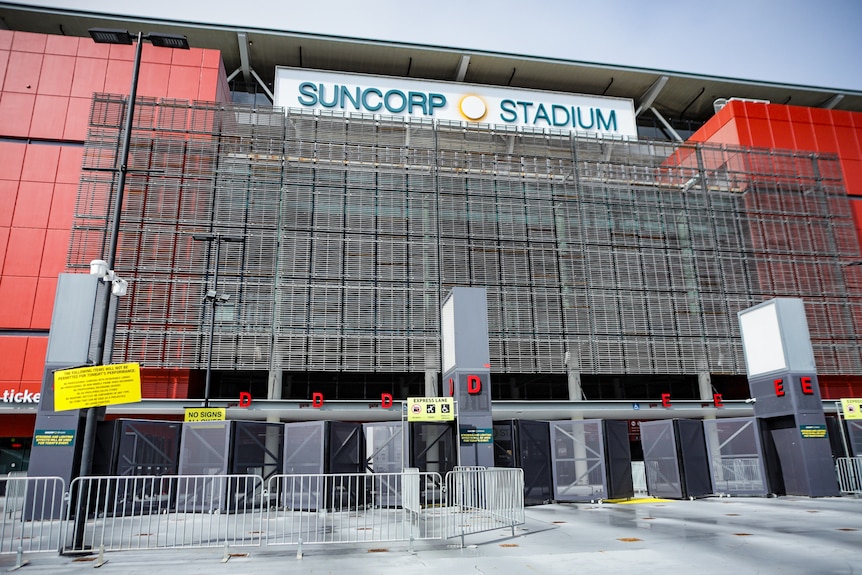 The front gates of a stadium. temporary fencing around the entrance. A alrge sign at the top that says: SUNCORP STADIUM.
