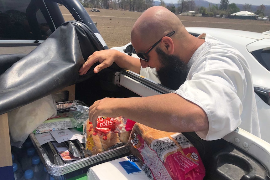 A man gets food out of the back of a ute