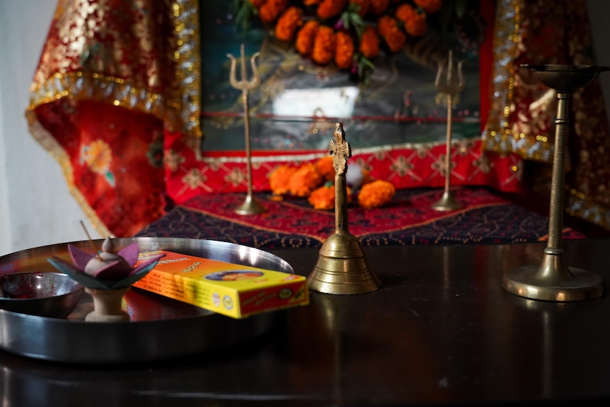 A packet of incense and several brass ornaments sit on a tray in front of an ornate tapestry