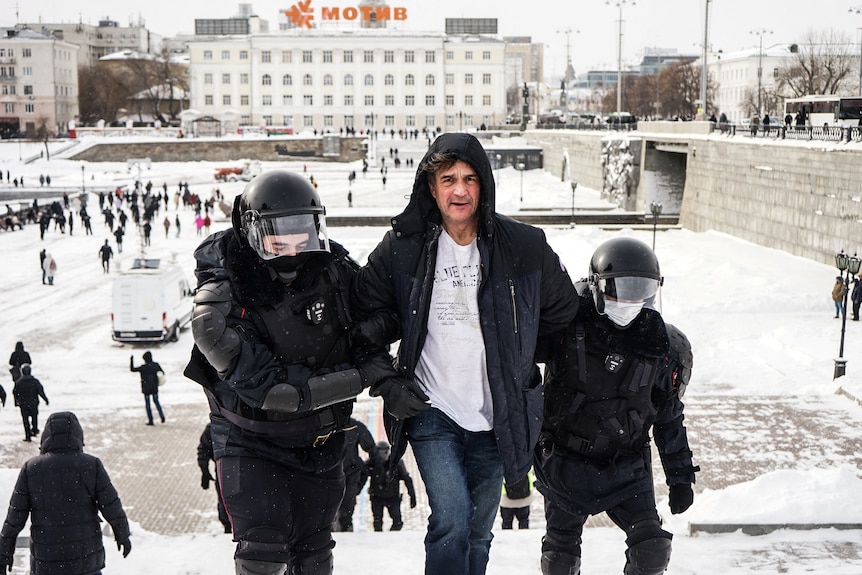 A man is held either side by two riot police officers.