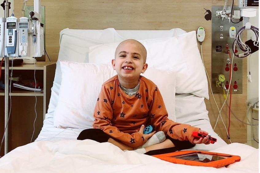 A young boy in orange pyjamas in a hospital bed.