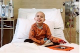 A young boy in orange pyjamas in a hospital bed.