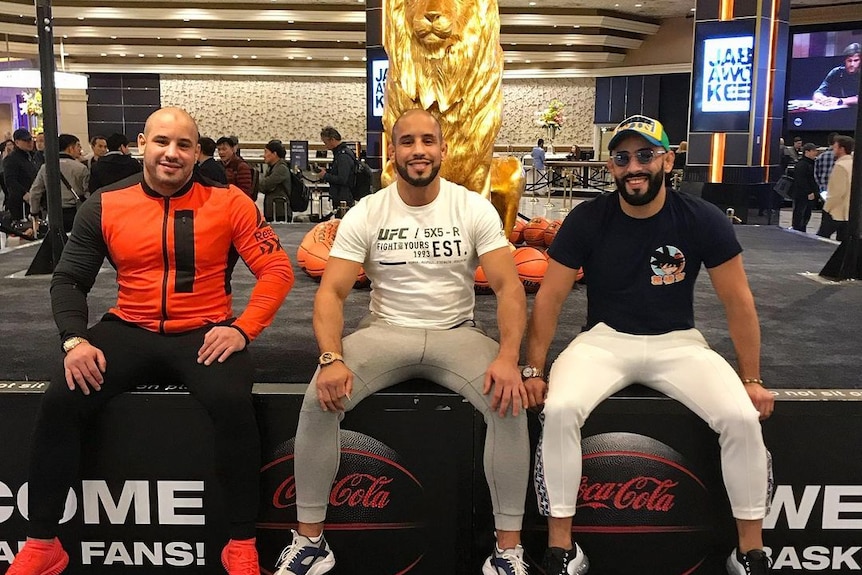 Three muscular men sitting on a bench at a gym 