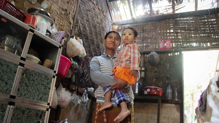 A mother and her child stand in their living room where you can see the sky through the roof