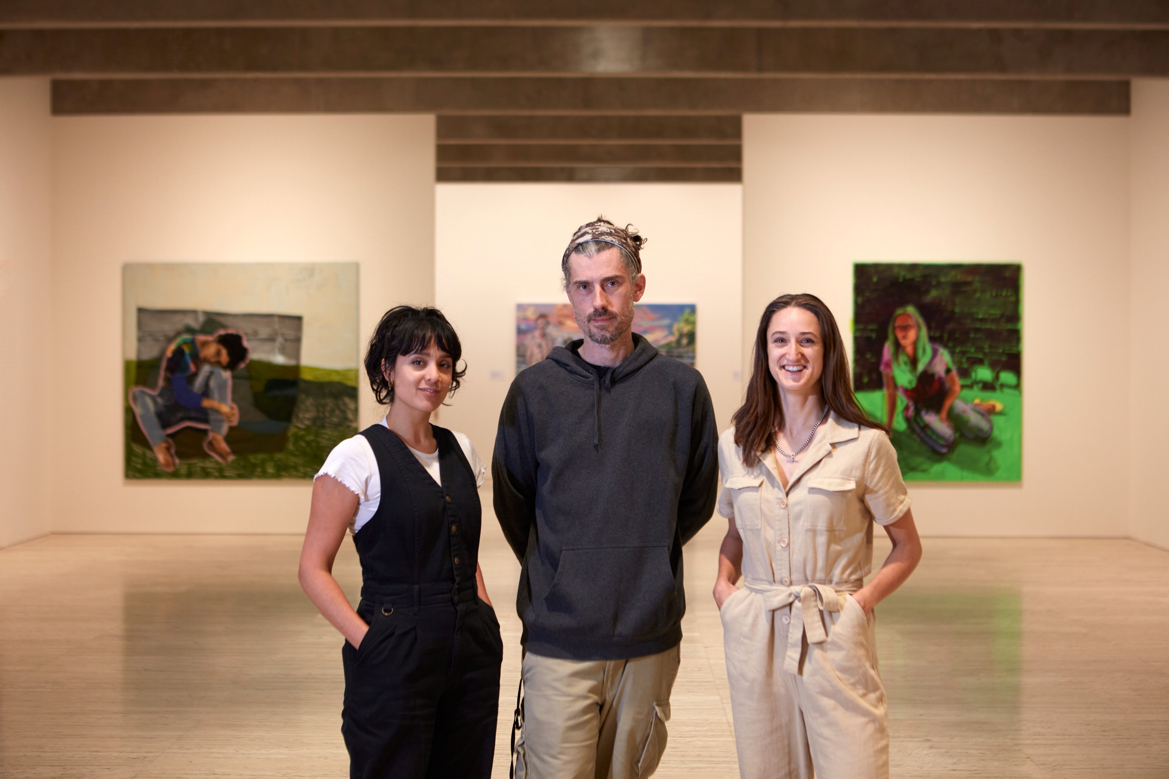 Two women and a man stand in front of portraits in an art gallery.