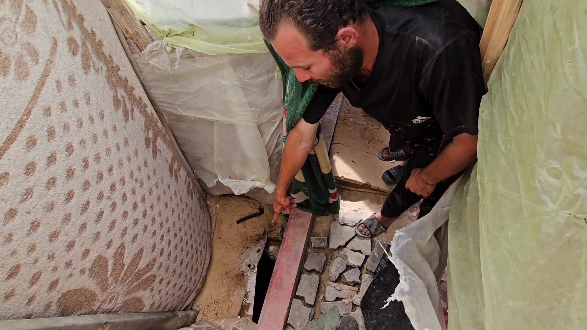 A man stands in a small covered area and points to a hole in the ground