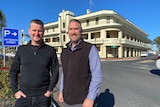 Two men stand across a road from a historic hotel building. 