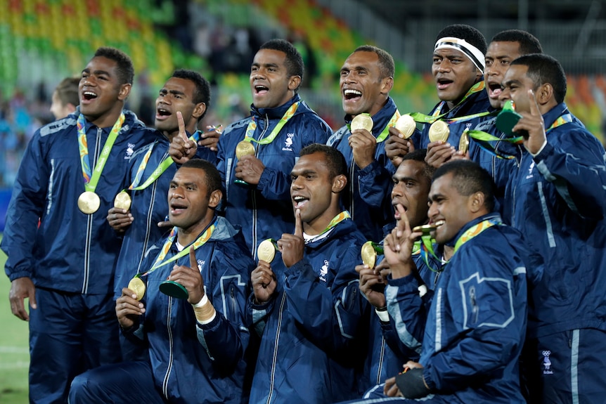 Men in green sports outfits hold up medals around neck and smile to the left of frame.