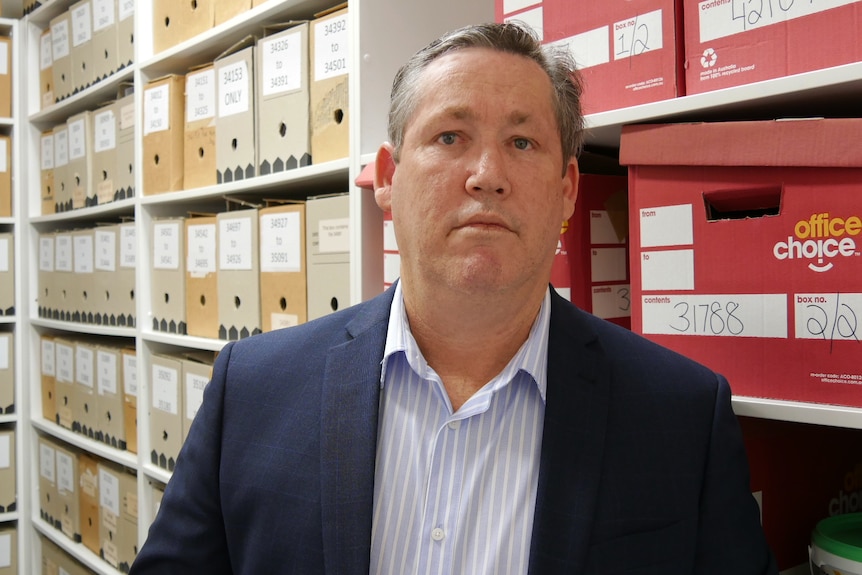 A profile shot of a man in a suit in a room full of boxes.