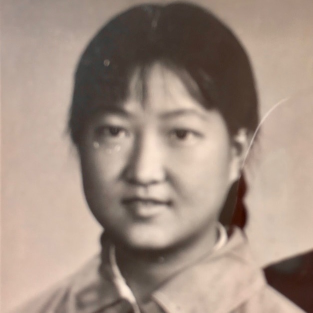 A girl wearing a shirt with her hair tied back looks at the camera in a sepia portrait photo.