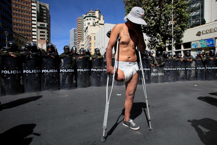 A demonstrator with a physical disability stands in front a riot police barricade.