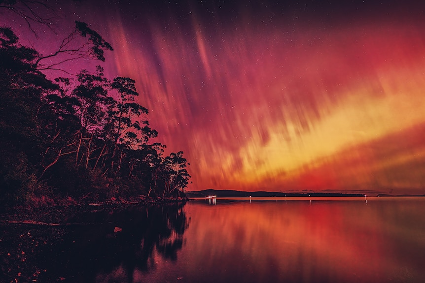 Aurora Australis lighting the sky pink, orange and yellow over a river
