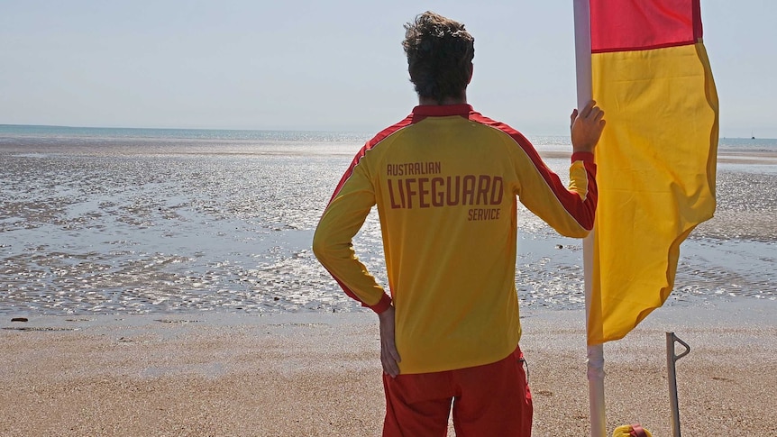 Lifeguard standing with flag on Mindil Beach, Darwin.