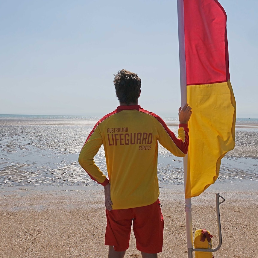 Lifeguard standing with flag on Mindil Beach, Darwin.
