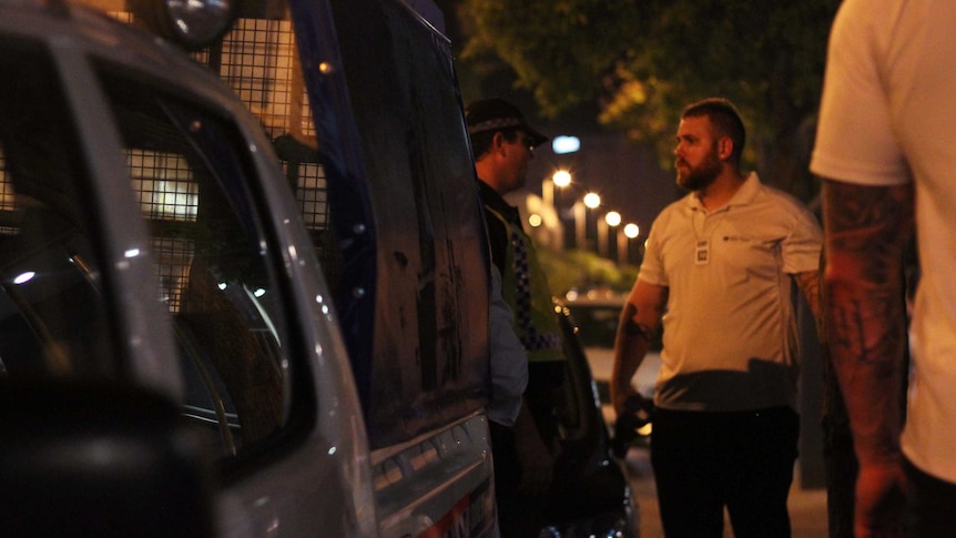 A bouncer talks to a police officer on a footpath at night.