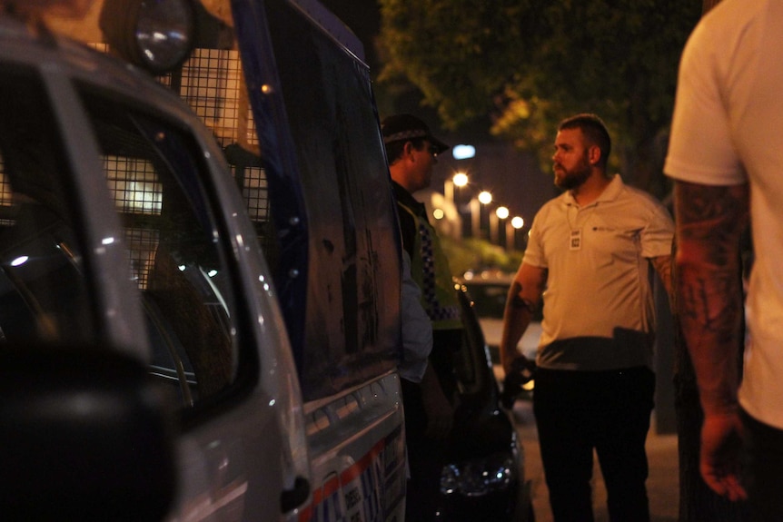 A bouncer talks to a police officer on a footpath at night.
