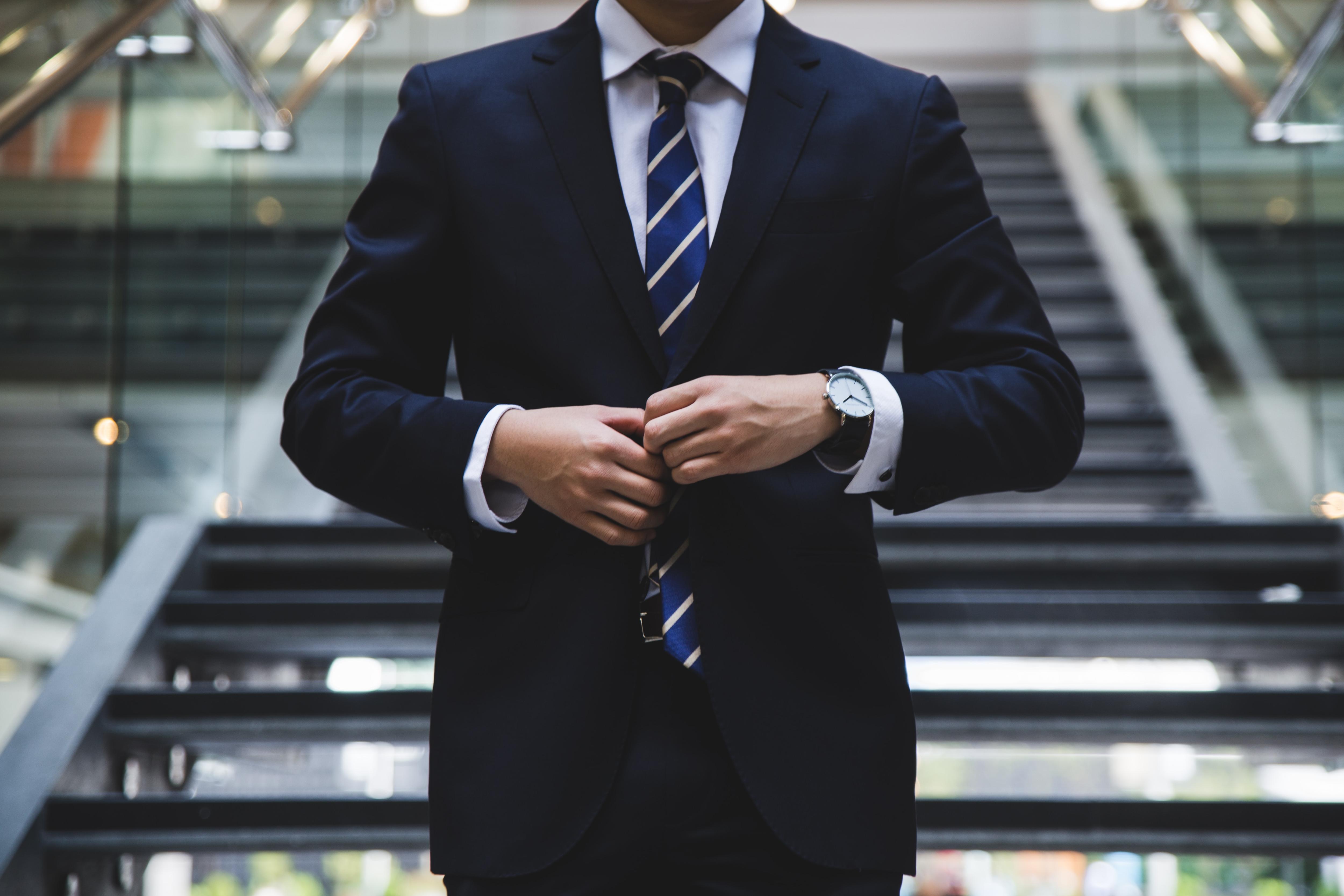 Close up of a person from neck to waist wearing dark blue suit and tie and holding their jacket at the buttons.