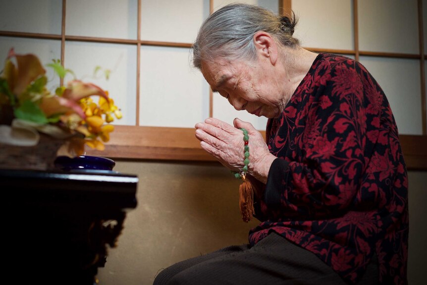 Setsuko kneeling in prayer with jade beads wrapped around her hands