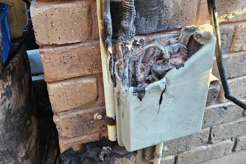 A burnt out plastic box on the side of a brick wall outside.