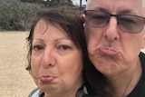 A close-up shot of a frowning couple with the SA-WA border sign behind them.