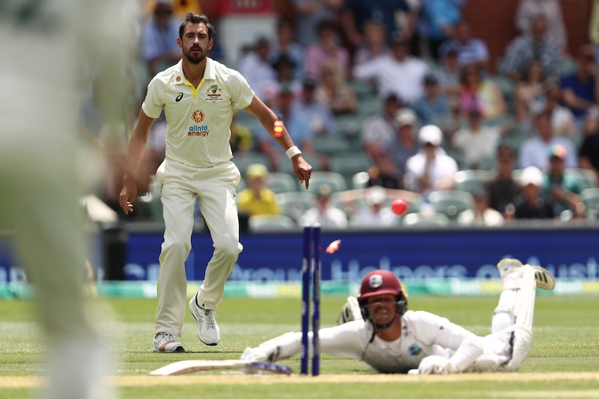 A West Indies batsman lies prone on the pitch as the bails fly off the stumps after the bowler runs him out.