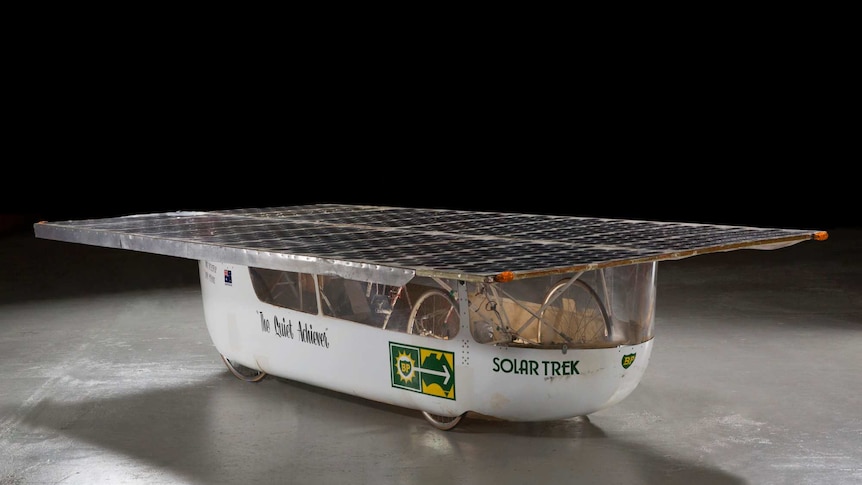 Solar car with flat top roof and The Quiet Achiever on the side on a black background