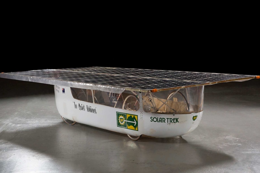 Solar car with flat top roof and The Quiet Achiever on the side on a black background