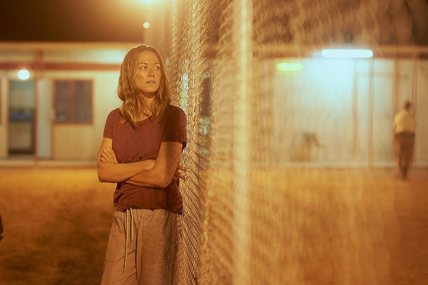 Yvonne stands, arms folded, leaning against a wire fence.