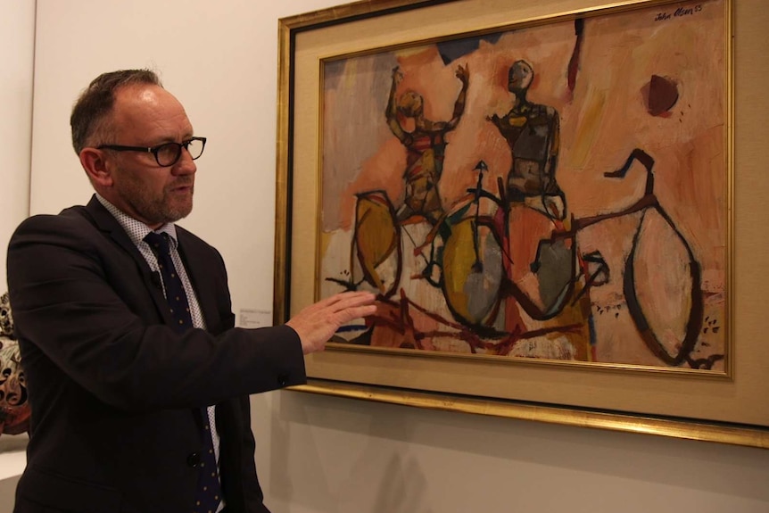 A man points at something in a painting of figures on bikes
