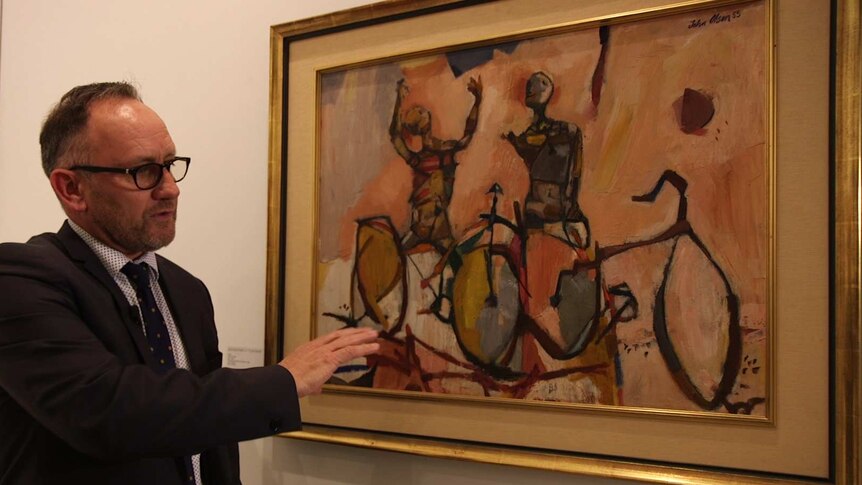A man points at something in a painting of figures on bikes