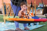 A one year old boy with brown hair and a orange patterned shirt sits on a swing being pushed by his mum in his backyard 