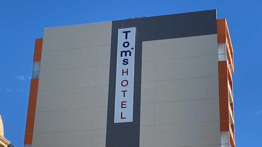 A multi-storey grey hotel building with Tom's Hotel written vertically on a sign