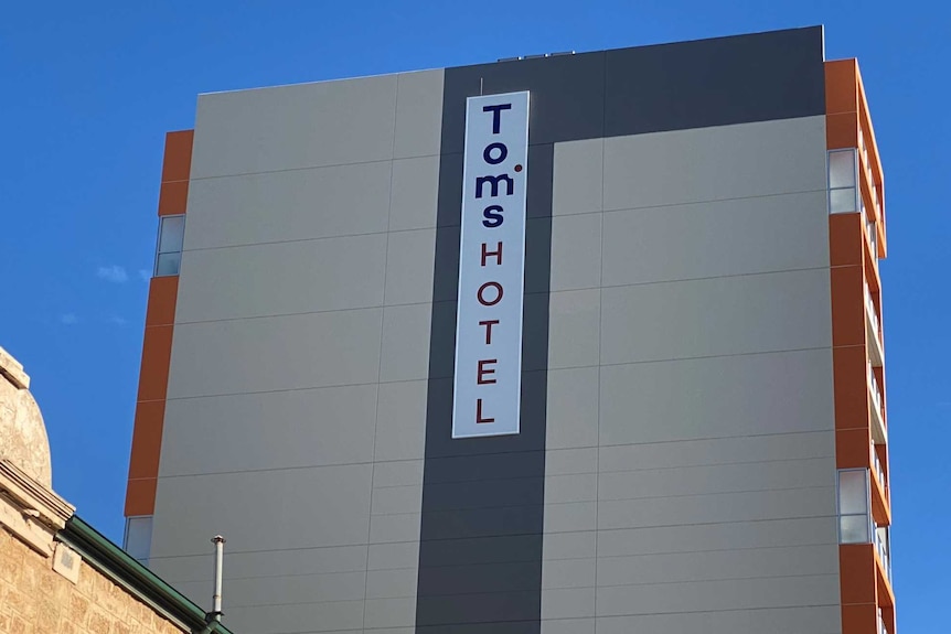 A multi-storey grey hotel building with Tom's Hotel written vertically on a sign