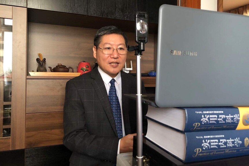Xiao Jinsong sitting in front of his laptop, perched on top of thick books, for a video conference.