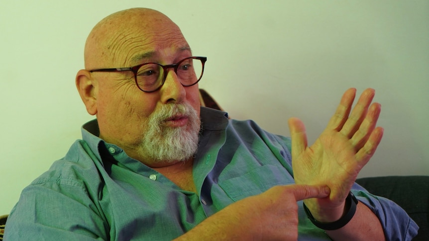 Barry Priori sitting down signing wearing a blue shirt and glasses