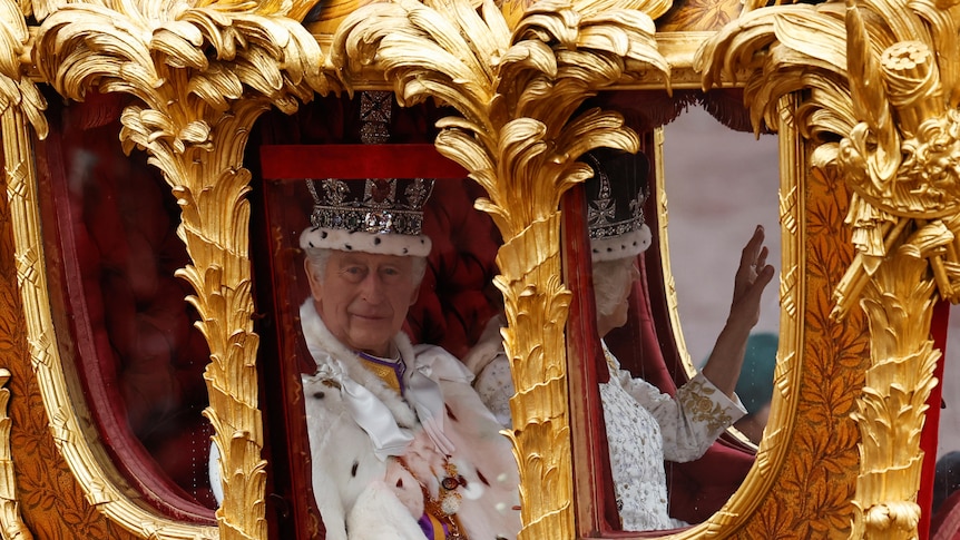 King Charles and Camilla seen through the windows of a gold carriage
