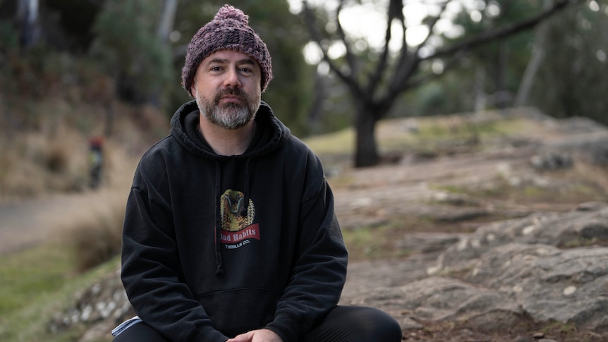 Man with greying beard wearing a beanie and hoodie, with serious expression, looks at camera 
