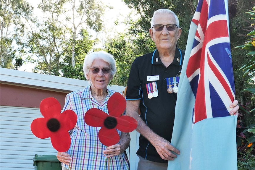 Roy Hartman and his wife Dawn stand in their driveway with a flag and paper poppy flowers.