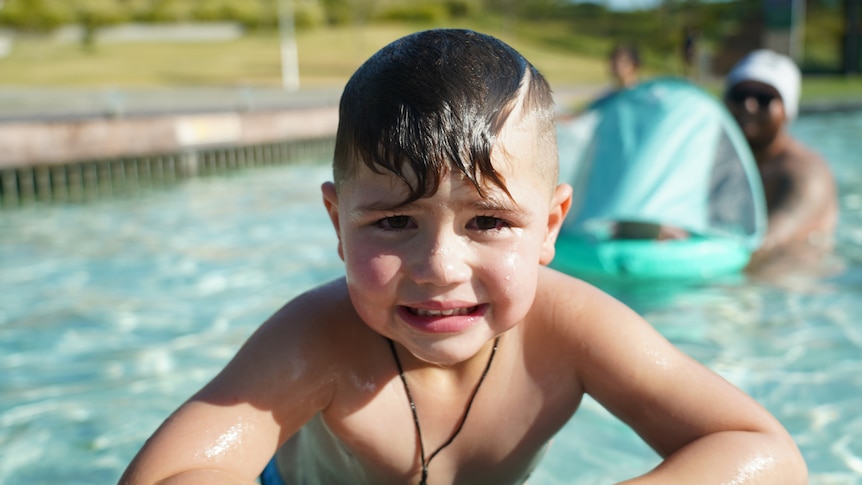 A young boy with dark hair leans out of a pool
